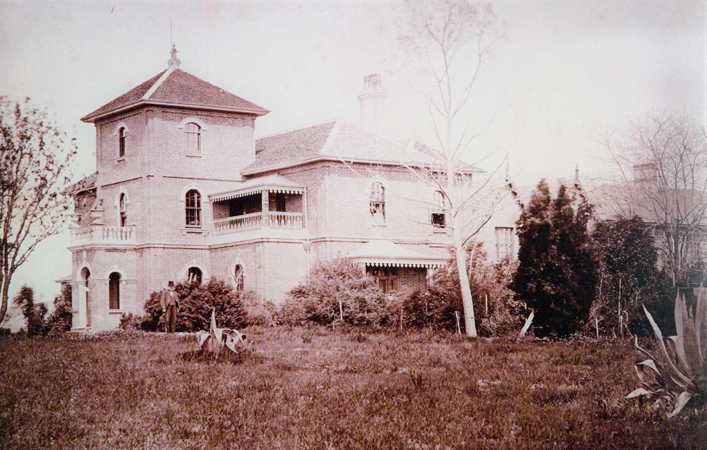 Photograph of homestead with lawn in front and a man standing in front of the house. - click to view larger image