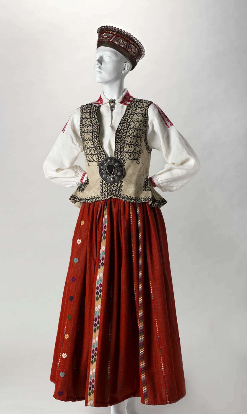 A mannequin dressed in a red skirt, cream coloured, embroidered waistcoast, white linen shirt and felt cap.