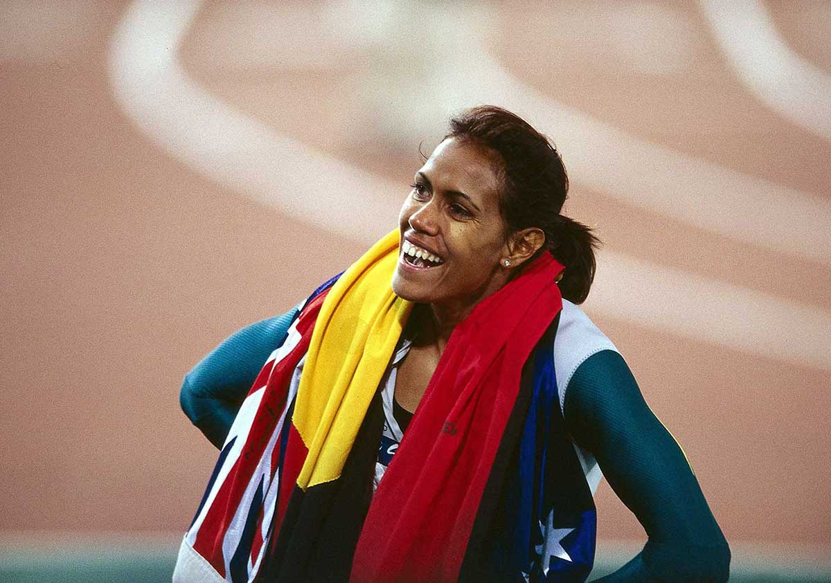 Cathy Freeman on the race track draped in the Australian and Aboriginal flags. - click to view larger image
