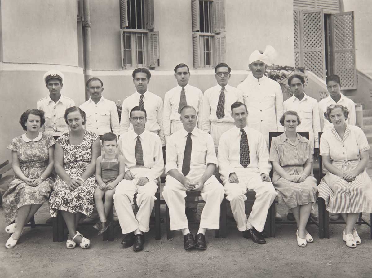 Large black and white photo depicting a group portrait of men, women and one child.