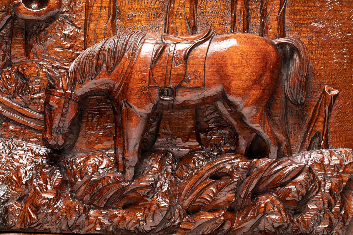 Detail of an ornate wooden panel of a relief carving of a horse feeding in bushland. - click to view larger image