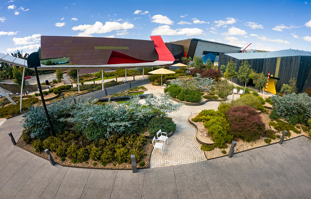 A view of a museum and its outdoor space featuring a well-maintained garden of Australian native plants, paved pathways, and seating for visitors.
