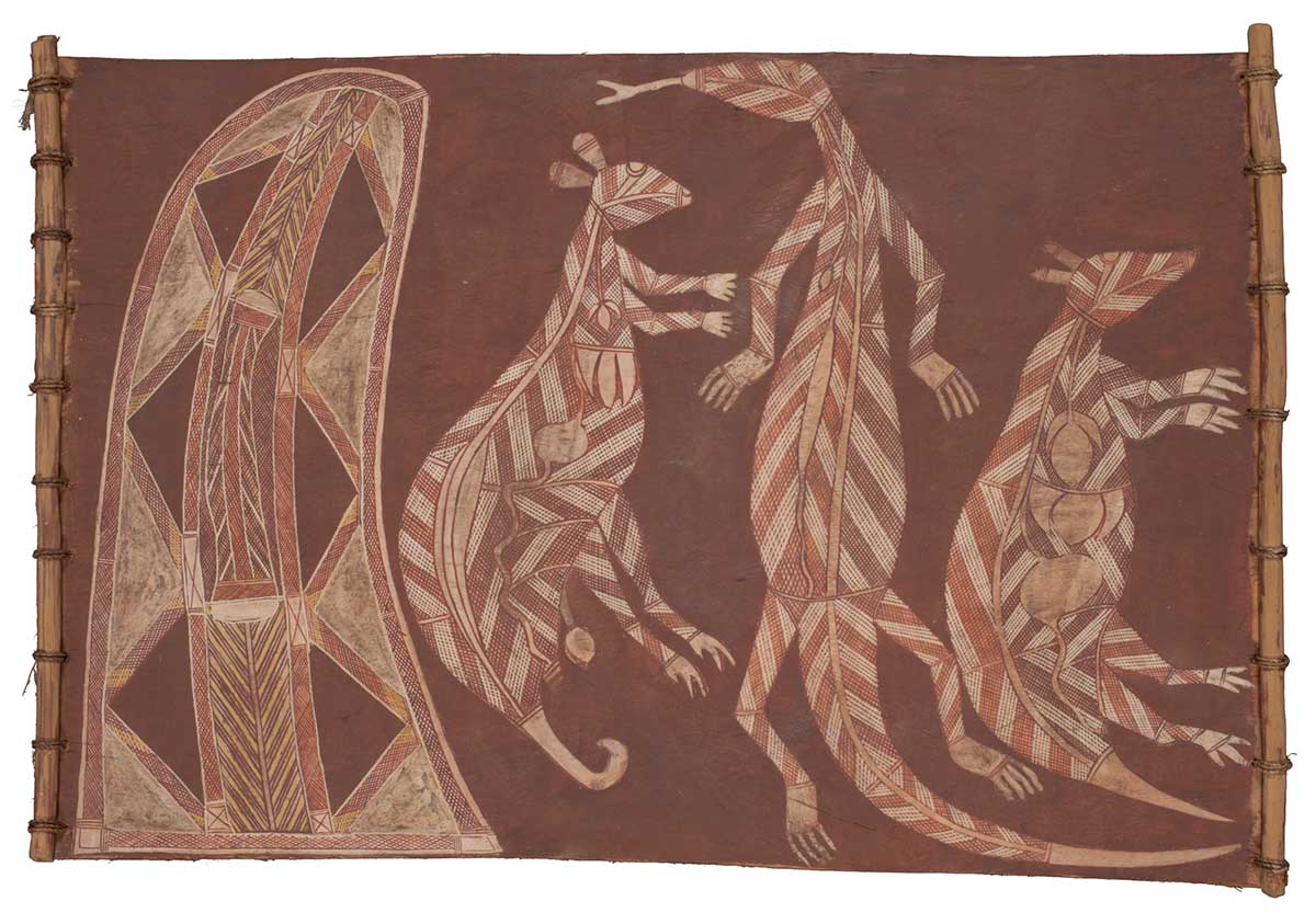 A bark painting worked with ochres on bark and on wooden restrainers. It depicts an elongated shape on the left and then a Northern Brown bandicoot, a sand goanna and a possum. The animals are painted in x-ray style with red and white crosshatching. The shape on the left has been painted as a pipeclay silhouette which rises to a point leaning towards the animals. A band of red cross hatching bordered by white lines surrounds an interior design of six red filled triangles, each bordered by bands of red and yellow hatching. The painting has a red background. - click to view larger image