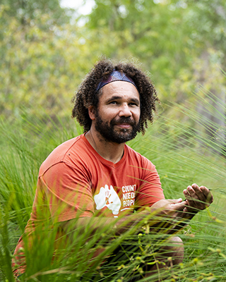 A photograph of Nathan Brennan. Nathan has brown curl hair with a headband, and a brown beard.