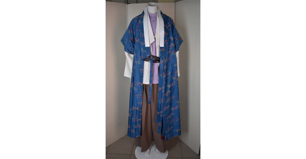 A standing mannequin, over which is placed an untucked, colllar-less lilac shirt, buttoned to the top. Over this is a looser white shirt, known as a jegori, and over this is a long blue outer layer known as a dapho. Long, loose brown pants.