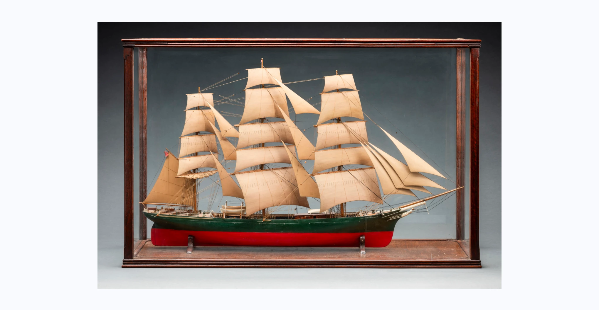  A model of a green and orange-red ship featuring three masts and three white lifeboats. Painted in white on both sides is the word 'THERMOPYLAE'. The ship is housed in a timber case with glass sides.