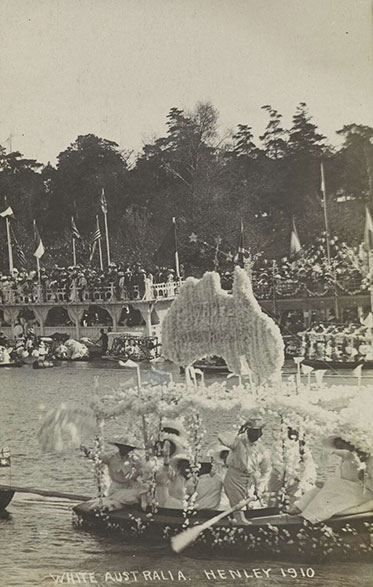 A boat with some kind of white structure supporting a white map of Australia. Six or seven people are on board dressed in white