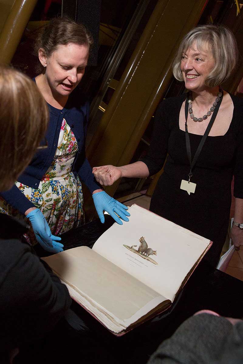 Two women with a large book, opened to show a sketch of small animals.
