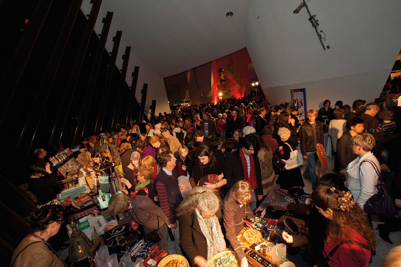 A photograph of a crowd attending a market inside a building.
