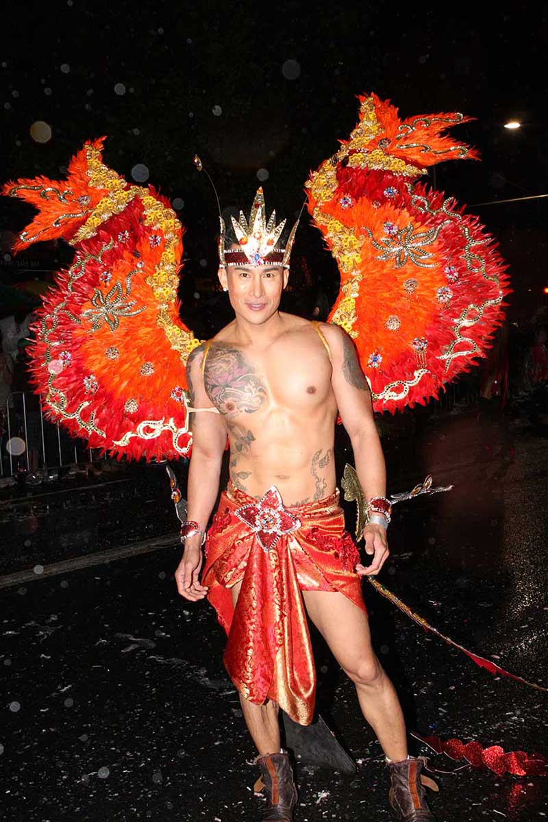 Tattooed man wearing orange dragon wings. - click to view larger image