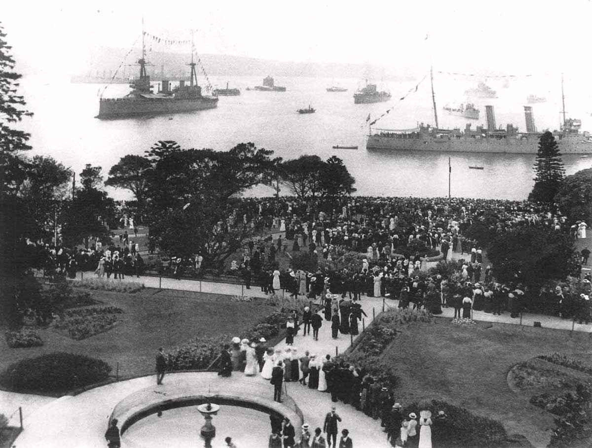 Two of that fleet unit’s warships and several smaller ones in background, with hundreds of people looking on from a park, possibly the Botanic Gardens.