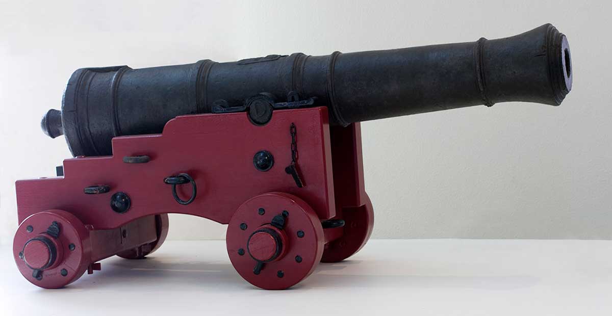 Iron cannon on a red painted wooden base with four wheels.