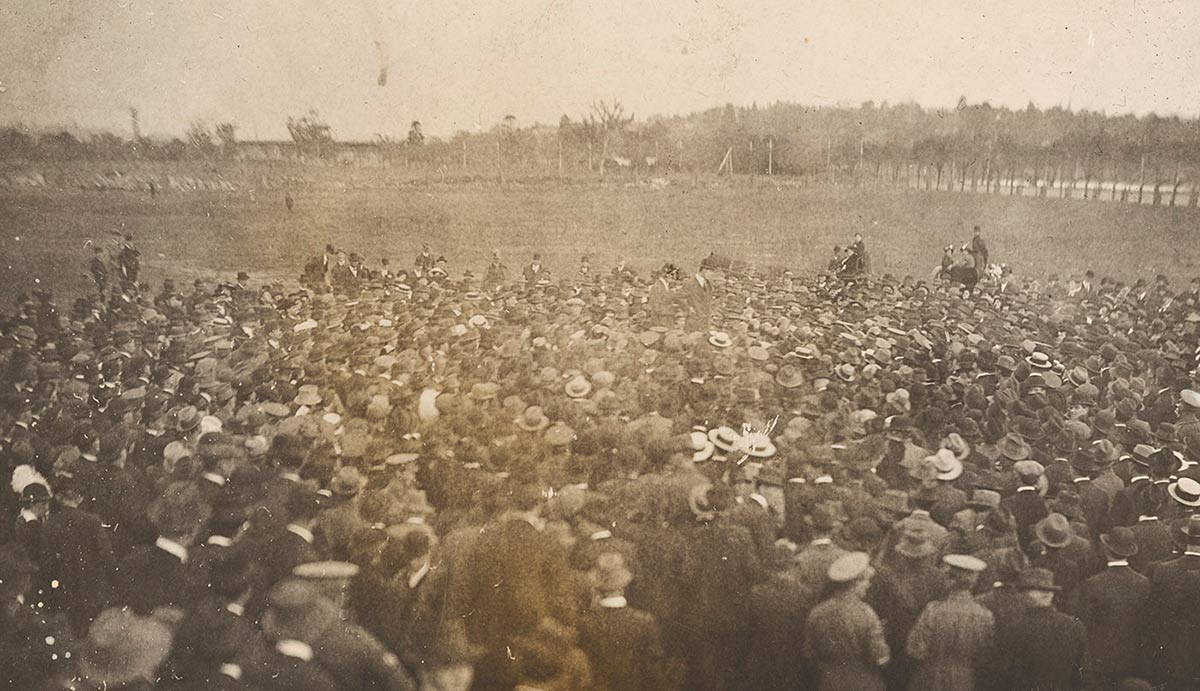 Grainy, poor-quality photo of a large crowd of men at an open expanse of grassland.