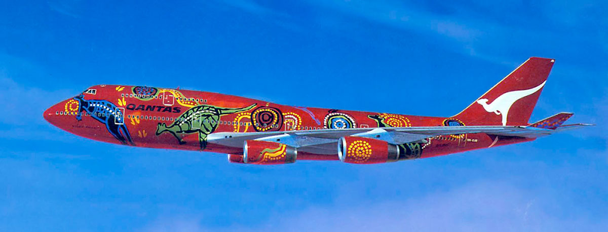 Side view of a large plane with Aboriginal designs painted on a red background. - click to view larger image