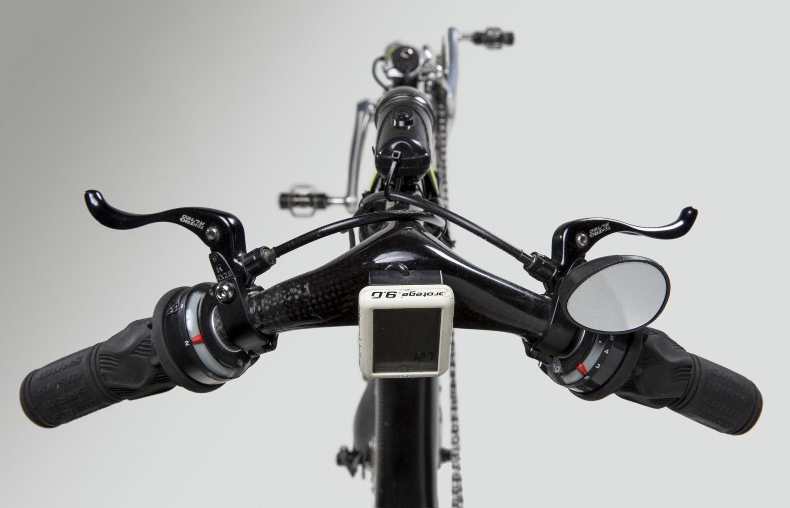 Colour photo, taken from above, showing a close up view of a bike's handlebars, with rubber handgrips and rear vision mirror. - click to view larger image