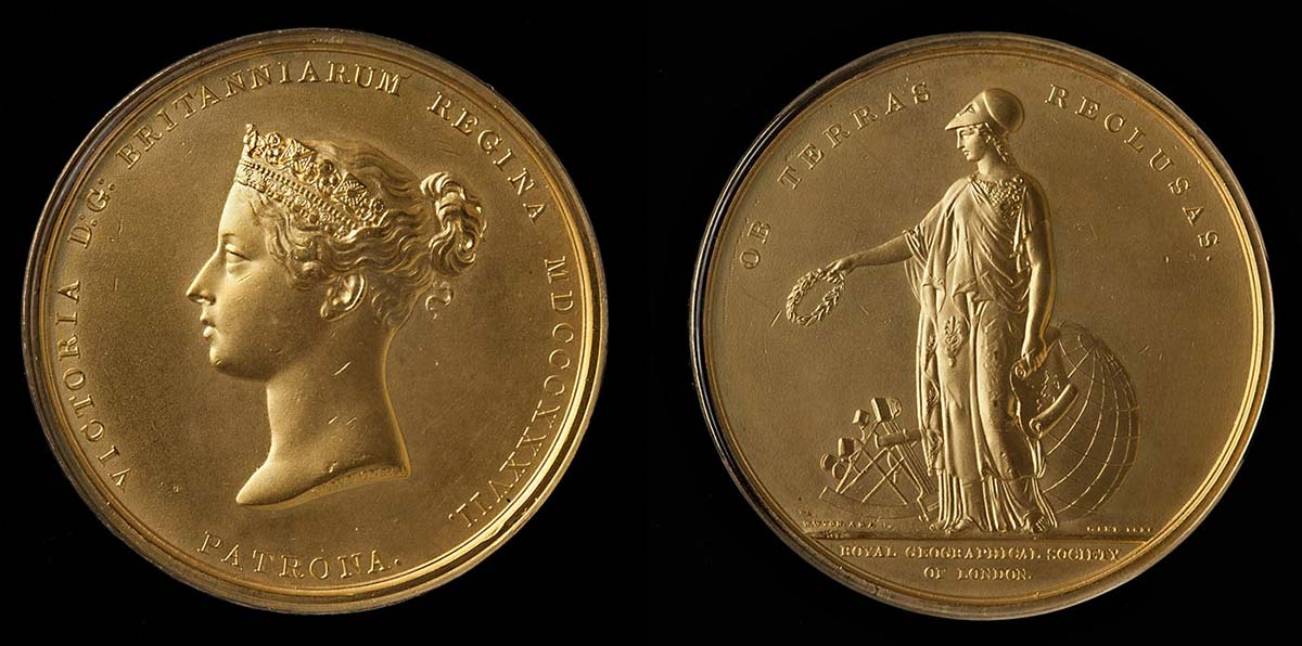 Image showing two sides of a gold medal on a black backdrop. The face on the left shows a figure of a woman with a laurel wreath in her right arm and a map in her left, with a sextant and globe behind her. The face on the right shows the profile of a woman wearing a crown.