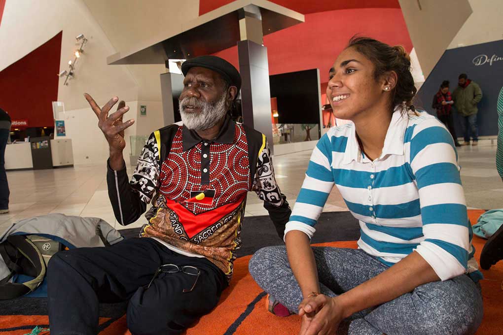 Elderly man sitting and in conversation with young woman.
