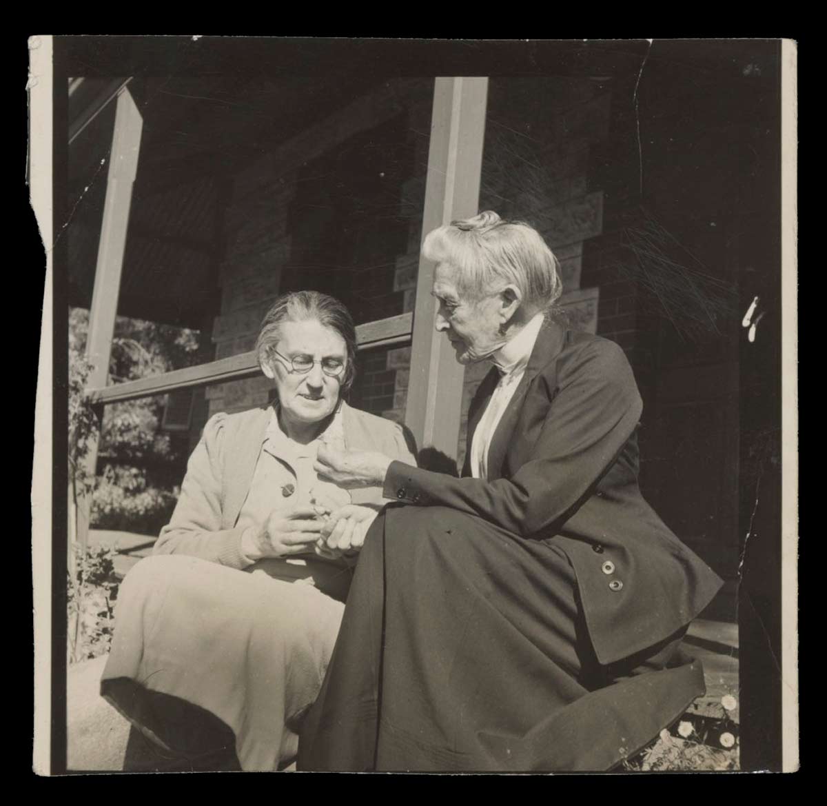Black and white photograph showing two women sitting on the step of a verandah. - click to view larger image