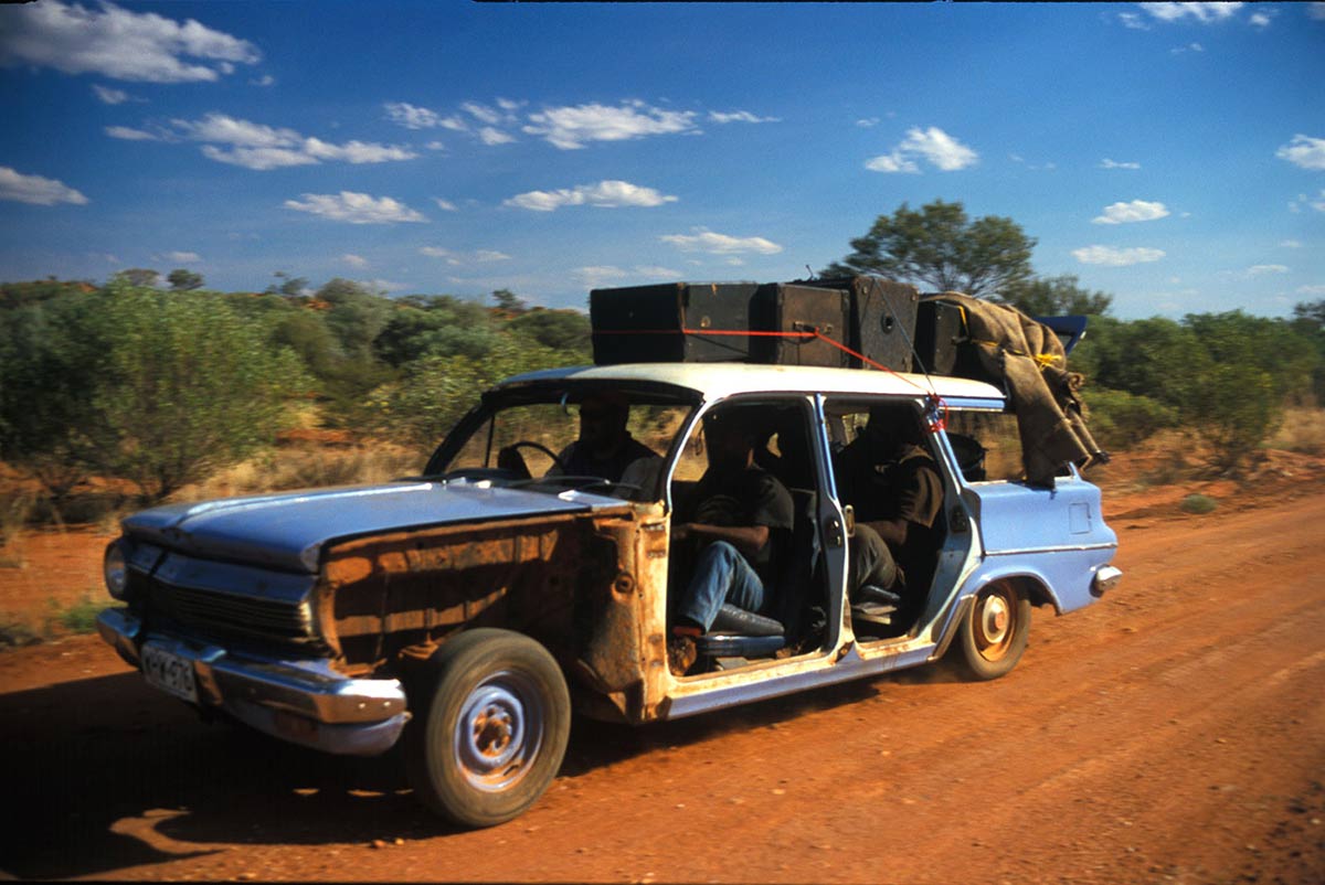 An EJ Holden with passengers travelling on a dirt road. - click to view larger image
