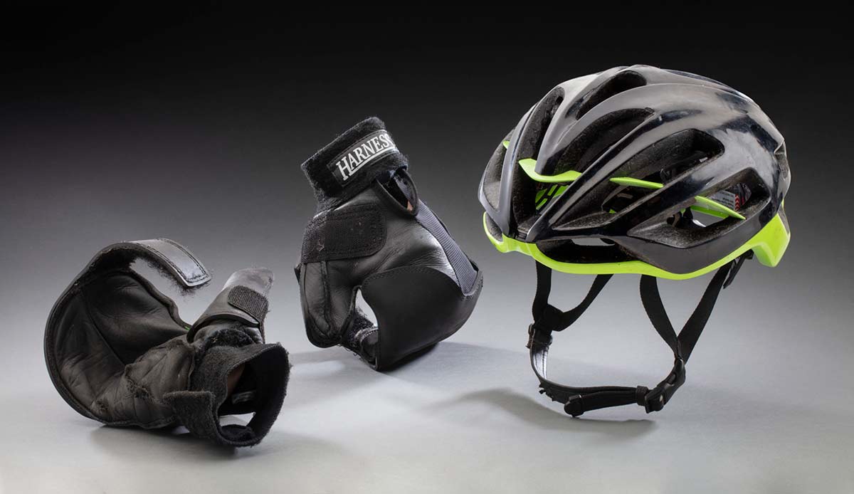 Two 'Harness' brand black cycling gloves beside a black cycling helmet with green trim.
