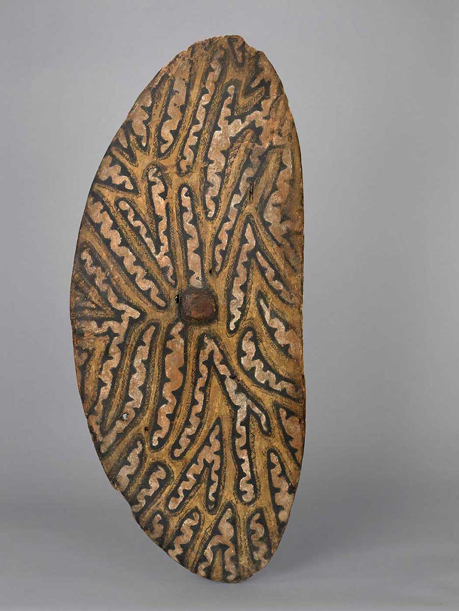 Ellipse-shaped bark shield featuring a yellow ochre design and a reddish-brown circle in the centre. - click to view larger image