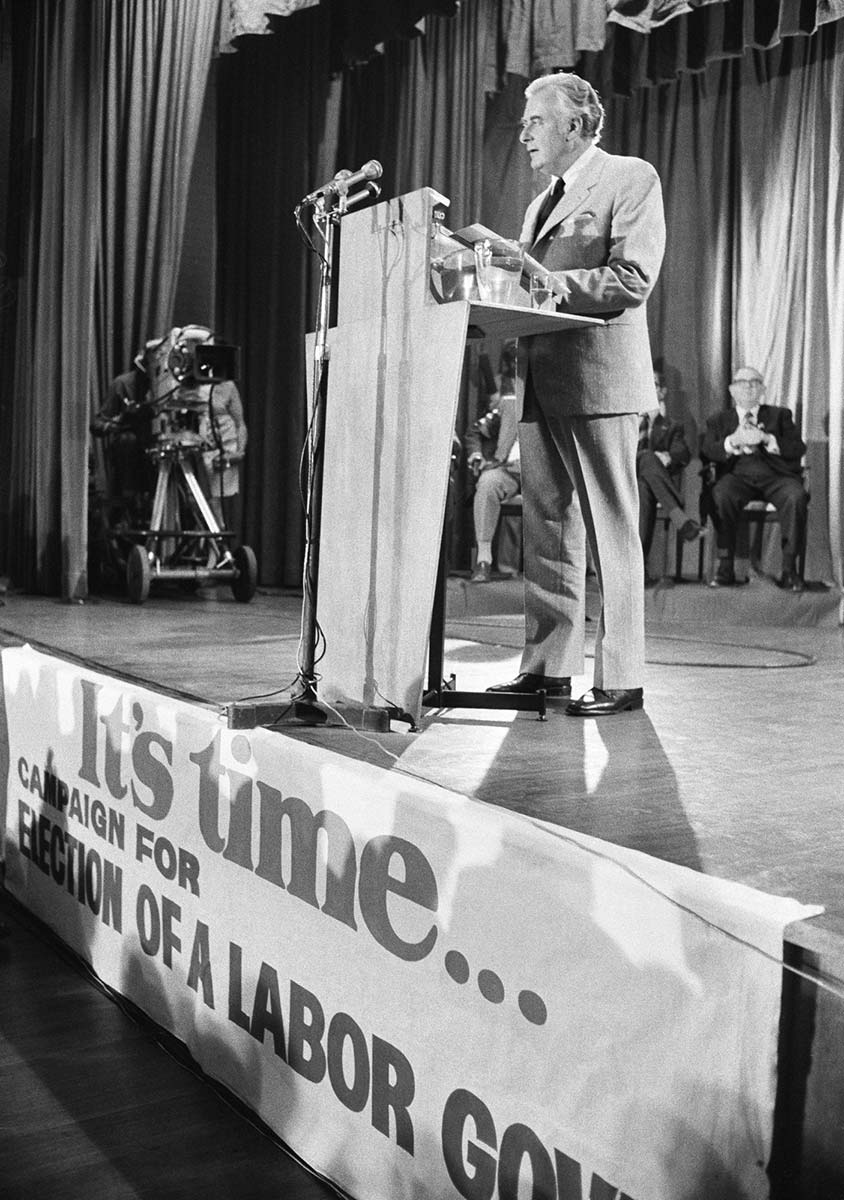 Black and white photo of Gough Whitlam giving a speech on stage. - click to view larger image