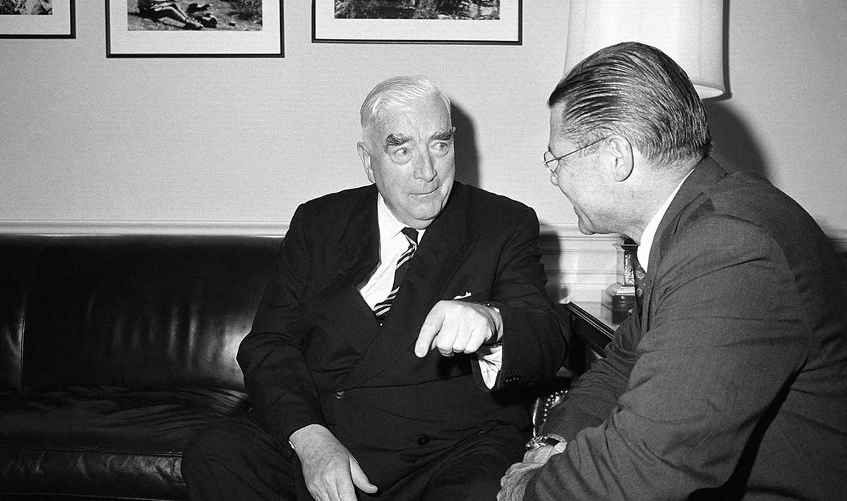 Interior photo of Robert Menzies seated on couch talking to a smiling Robert McNamara.