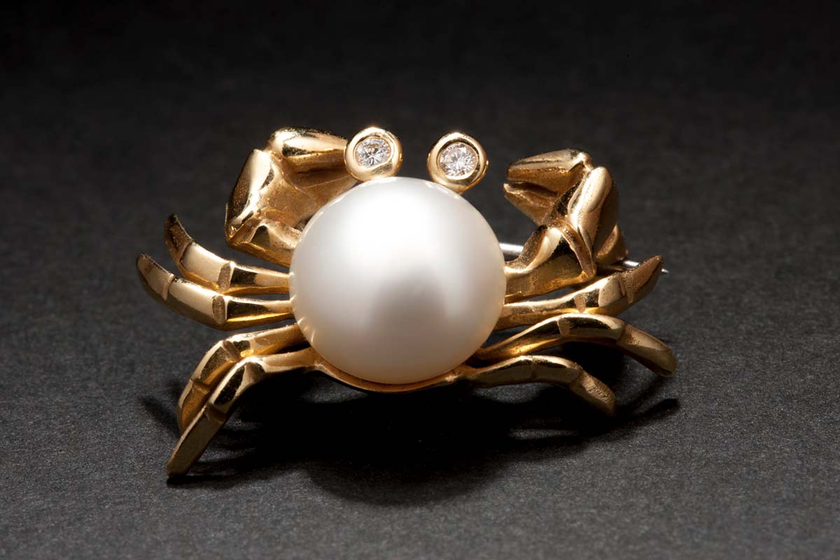 A gold coloured brooch in the shape of a crab with a pearl body and diamond-like eyes. - click to view larger image
