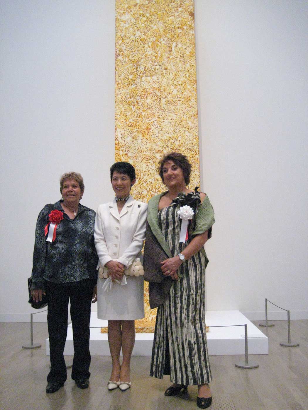 Three women standing in front of a painting. - click to view larger image