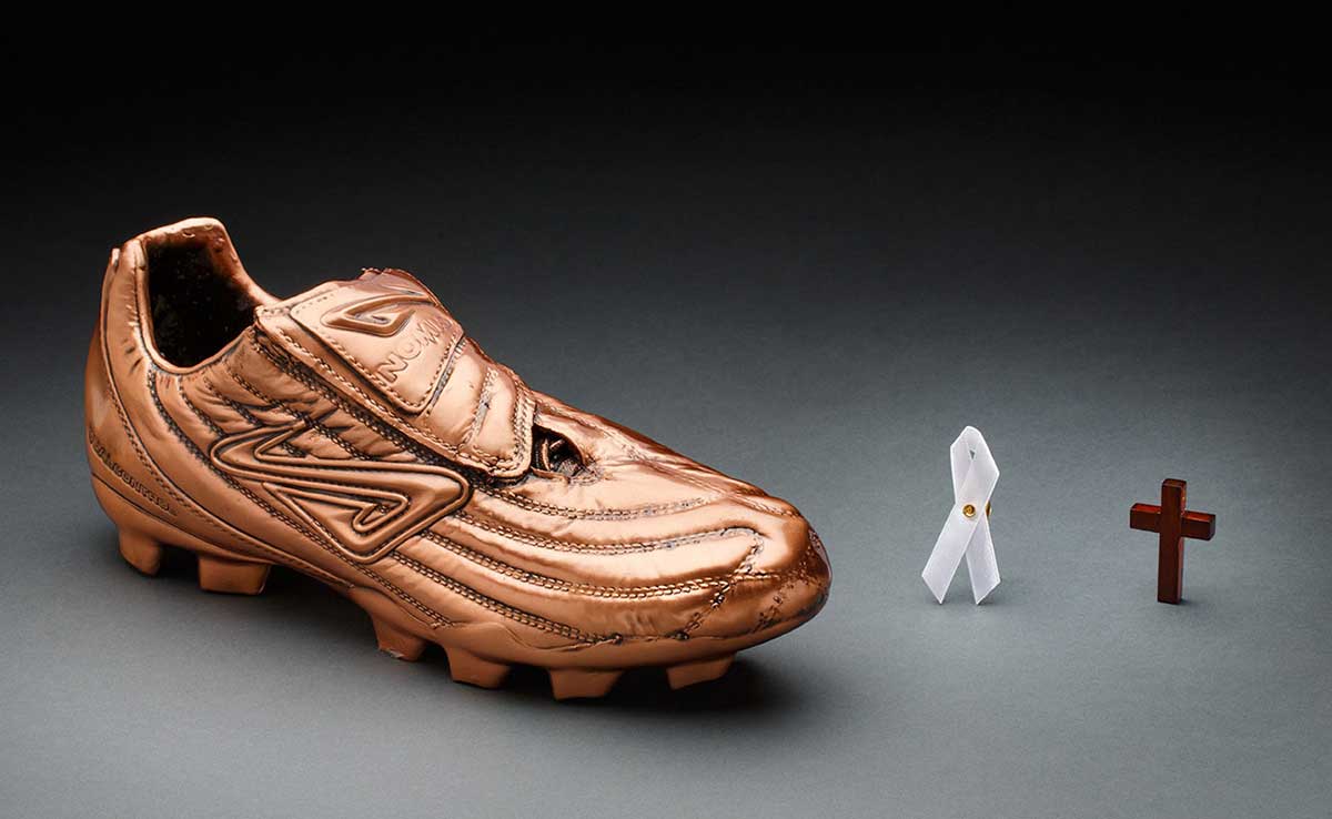 Bronze-coloured replica football boot, small white ribbon badge and small wooden cross - click to view larger image