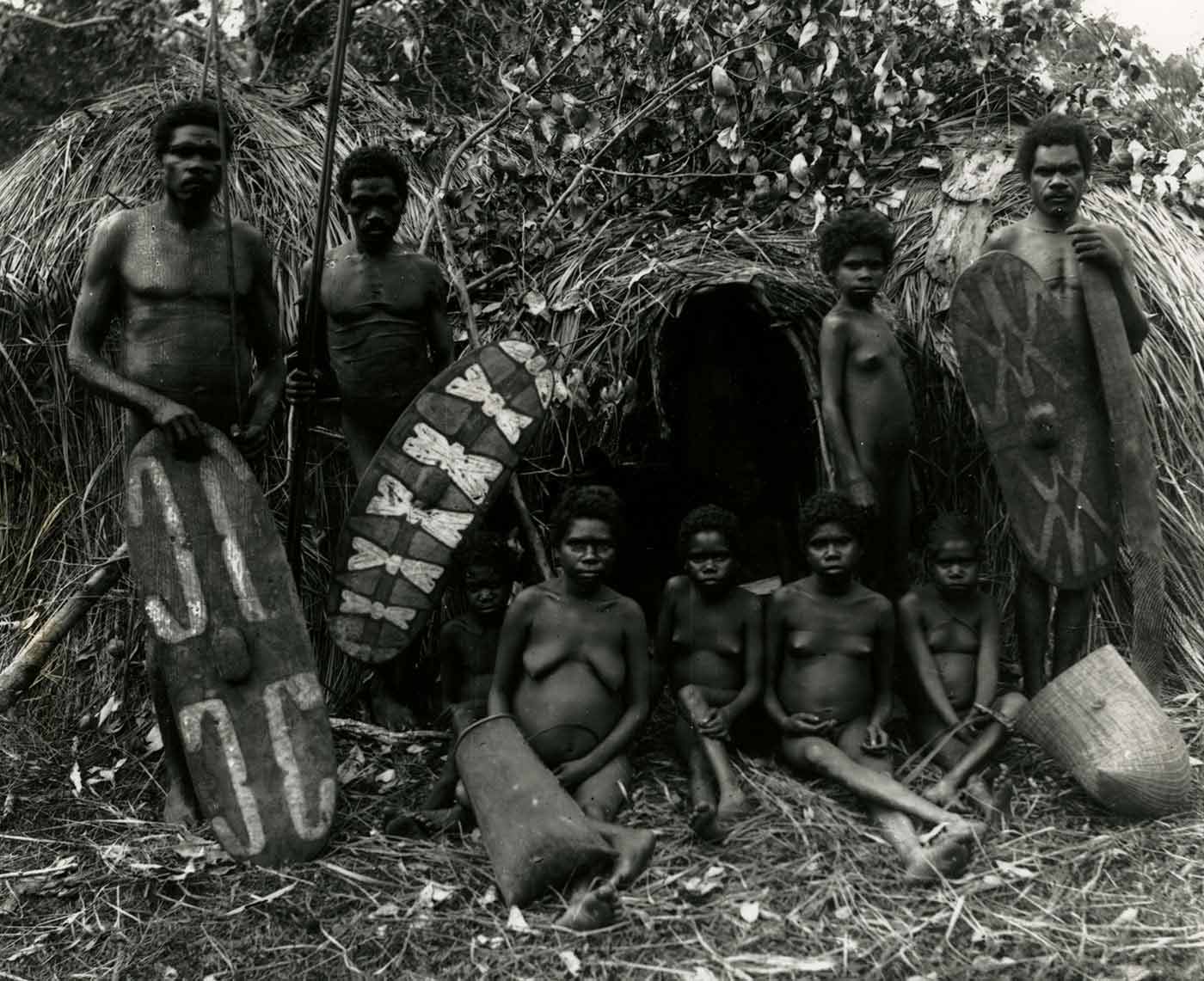A historic black and white photo of Indigenous Australian adults and children with their shields and baskets.