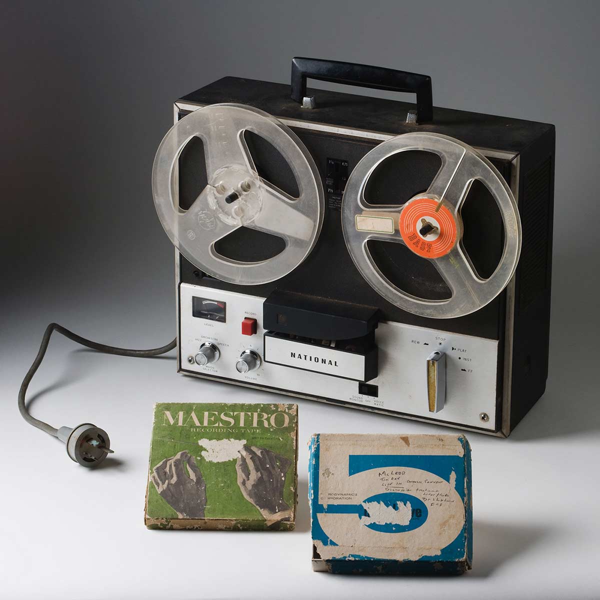 A 'NATIONAL' reel to reel tape recorder made from black plastic and silver coloured metal, with a power cable, a handle at the top, and a removable black plastic cover. - click to view larger image