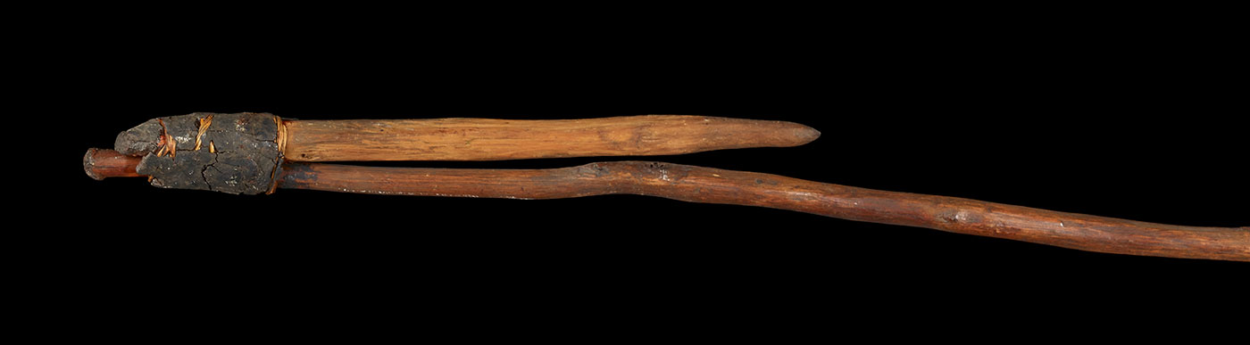 A hook consisting of a long wooden shaft, with a smaller length of wood attached so that protrudes at a slight angle. It is attached with wound fibre and gum.