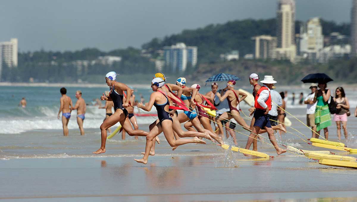 Female lifesavers running into the surf at the start of a race at the Australian Surf Life Saving Championships, Kurrawa, Queensland, 2006.
