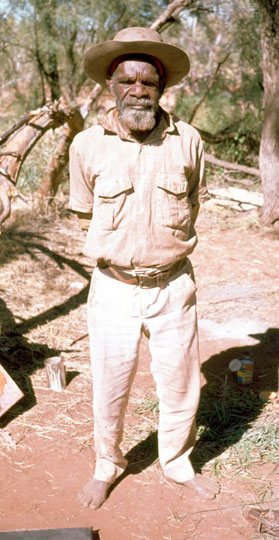 Portrait photo of an Aboriginal Australian man standing with his hands behind his back. - click to view larger image