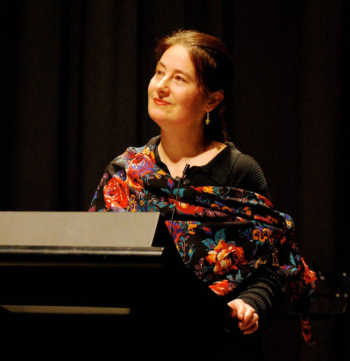 A woman stands at a lectern on a stage. - click to view larger image