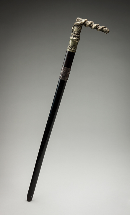 A riding crop with a silver L-shaped handle atop a black pole. - click to view larger image
