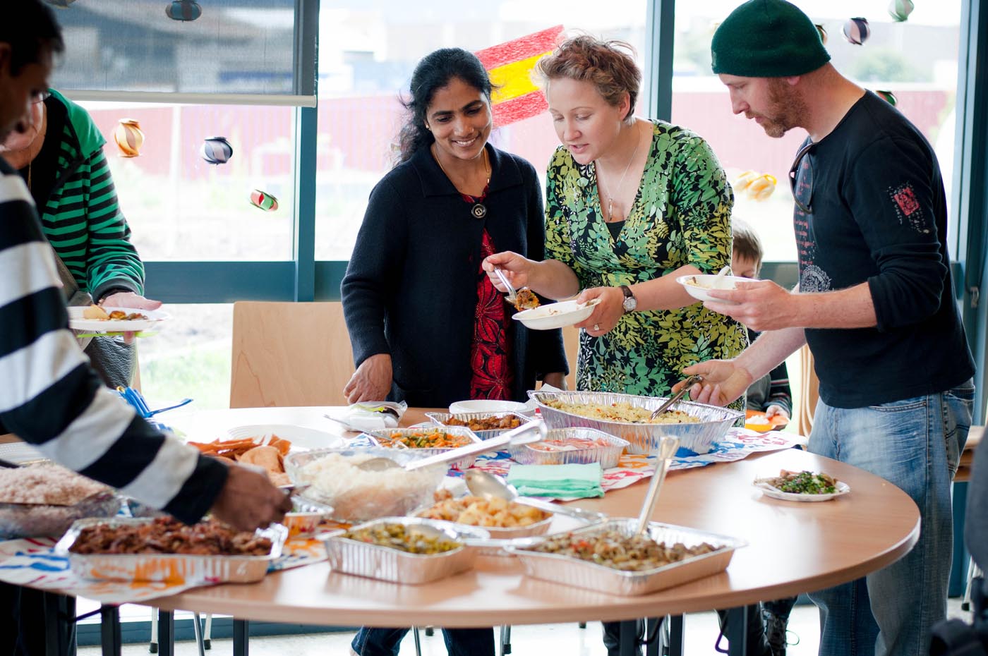 Photo of several people standing around a table helping themselves to food that is arranged in containers on the table - click to view larger image
