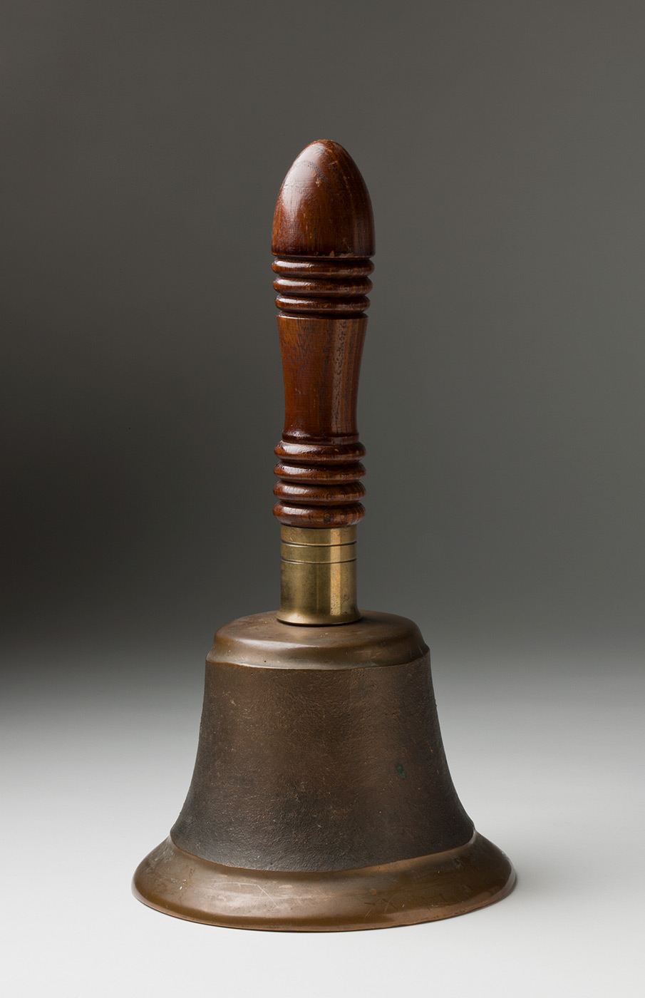 A colour photo of large metal hand bell with a wooden handle. - click to view larger image