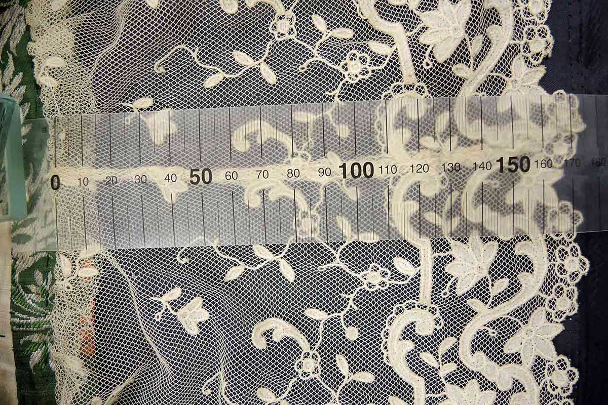 Close up of a tape measure lying over ornate lace detail. - click to view larger image