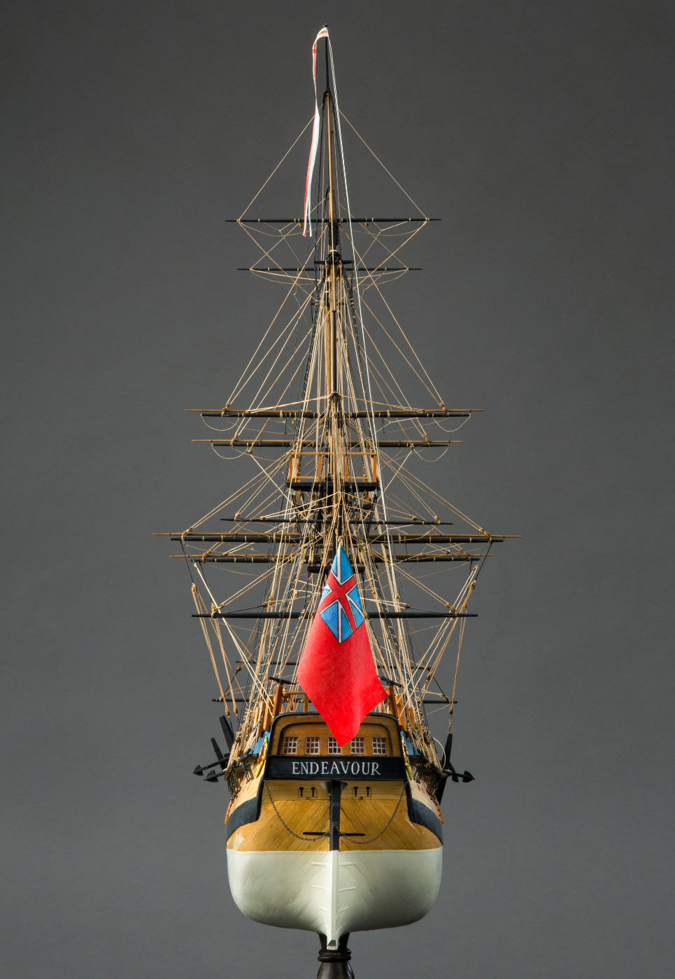 Rear view of a high-masted model wooden sailing ship, showing a red flag flying over the rear. - click to view larger image