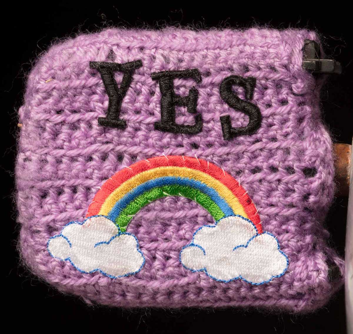 Studio photo of richly decorated pushbike pedal with the word 'YES' embroidered above an embroidered rainbow motif. - click to view larger image