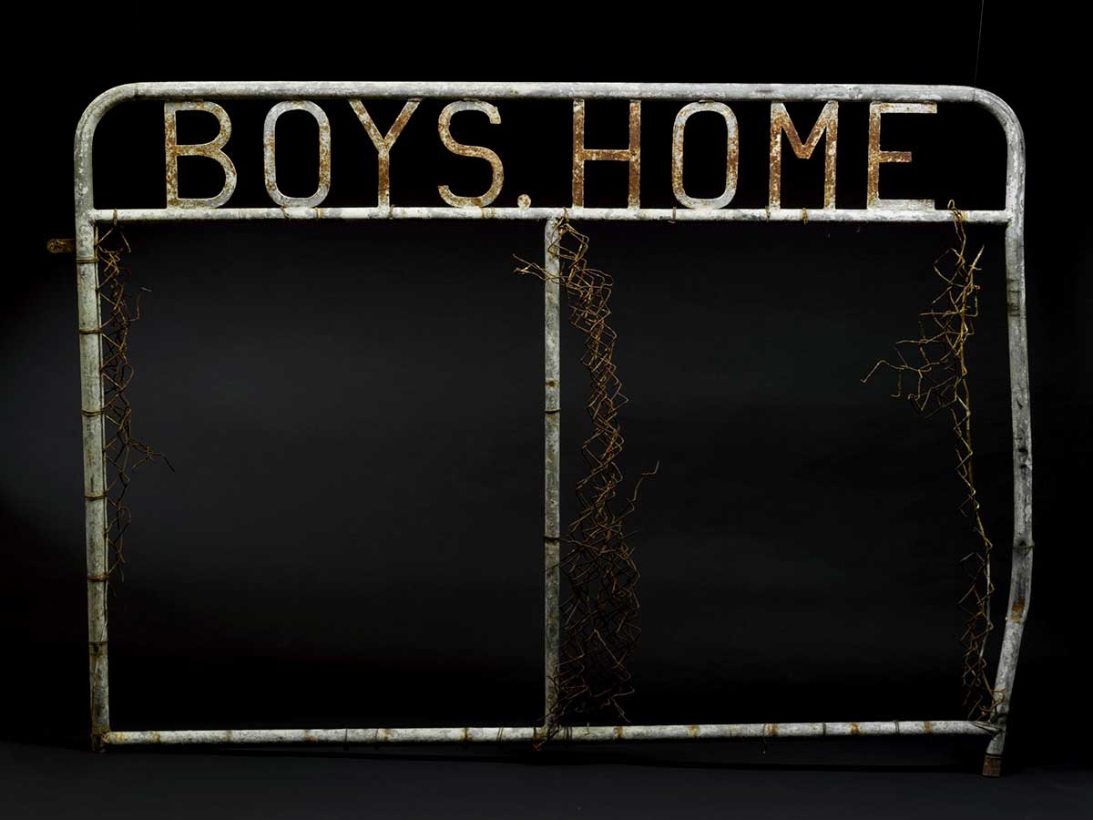 A metal gate with welded metal letters at the top which reads 'BOYS HOME'. - click to view larger image