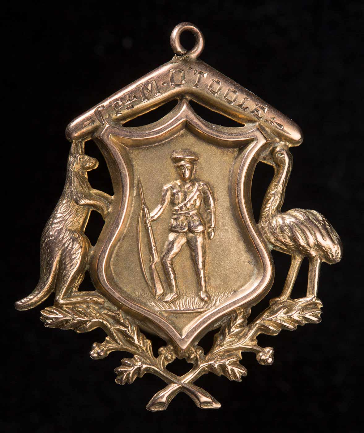 Fob medallion shaped as a shield flanked by a kangaroo and an emu with a boomerang and crossed sprays of wattle below. The boomerang is inscribed 