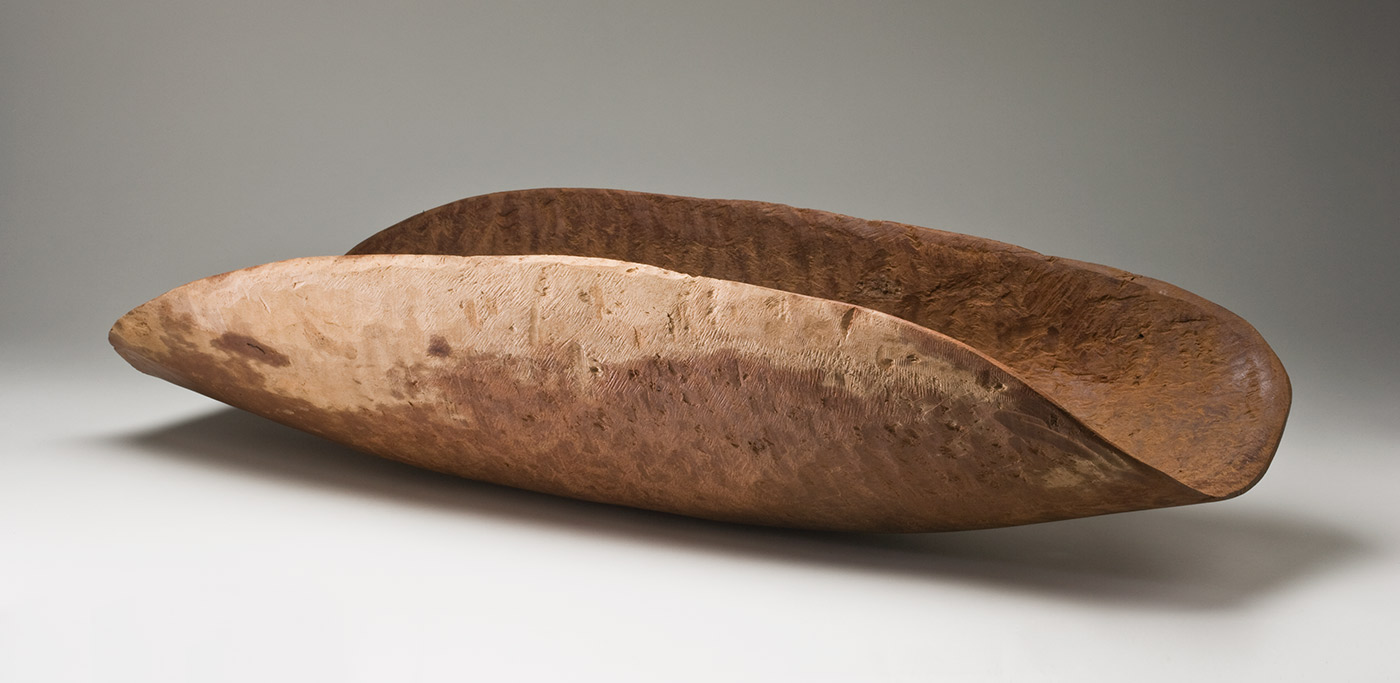 A large red-brown wooden concave oval container with drill holes in the surface and a pale patch of wood along one edge. The inner surface is rough and shows tool marks as well as drill holes with adhesive and sawdust around them. The outer surface is smoothed but shows the wavy grain of the wood. - click to view larger image
