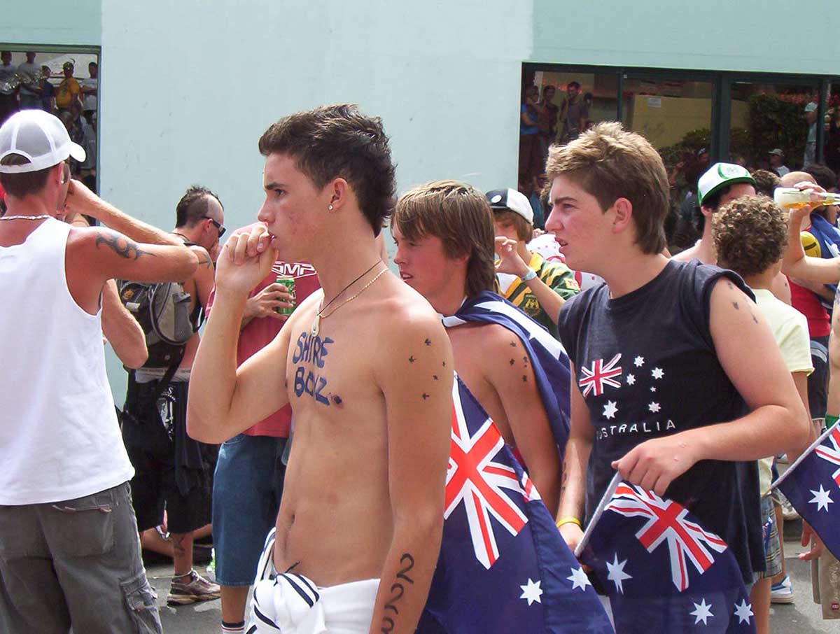 Colour photograph of a crowd of young male protesters with Australian flags, some drinking beer.