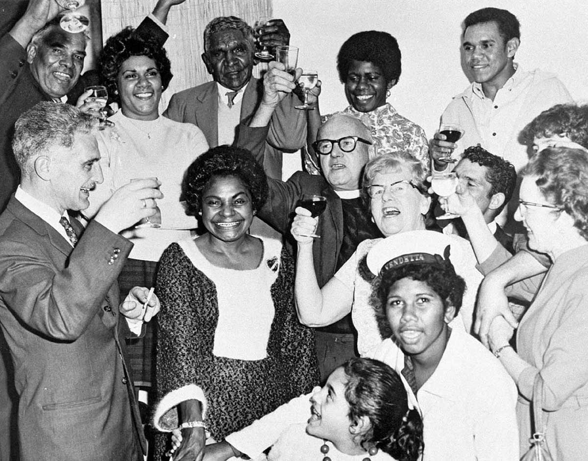 Black and white photo of a group of people cheering and raising their drinks in celebration.