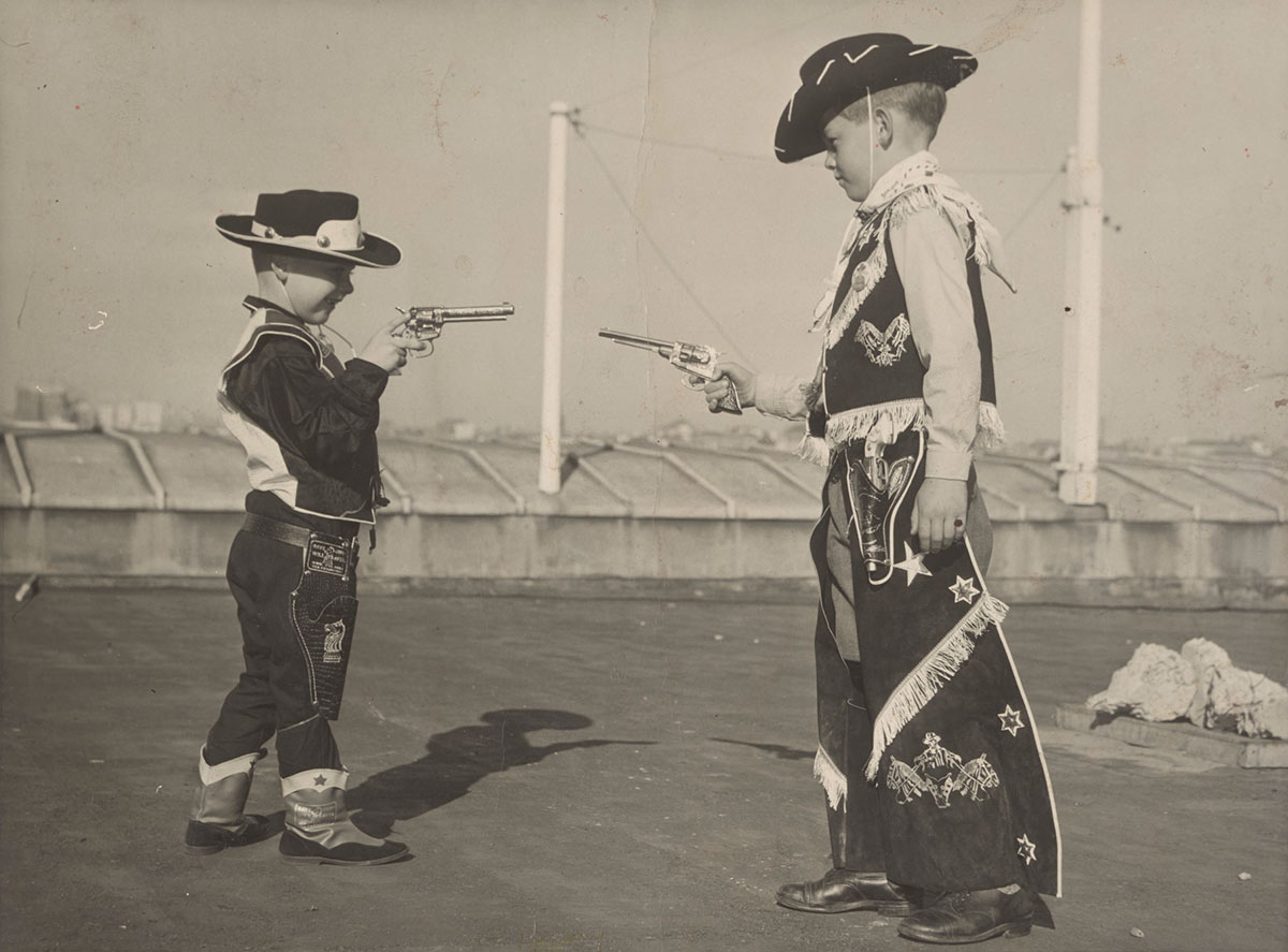 Black and white photograph of two young boys dressed in costumes and pointing toy guns at each other. - click to view larger image