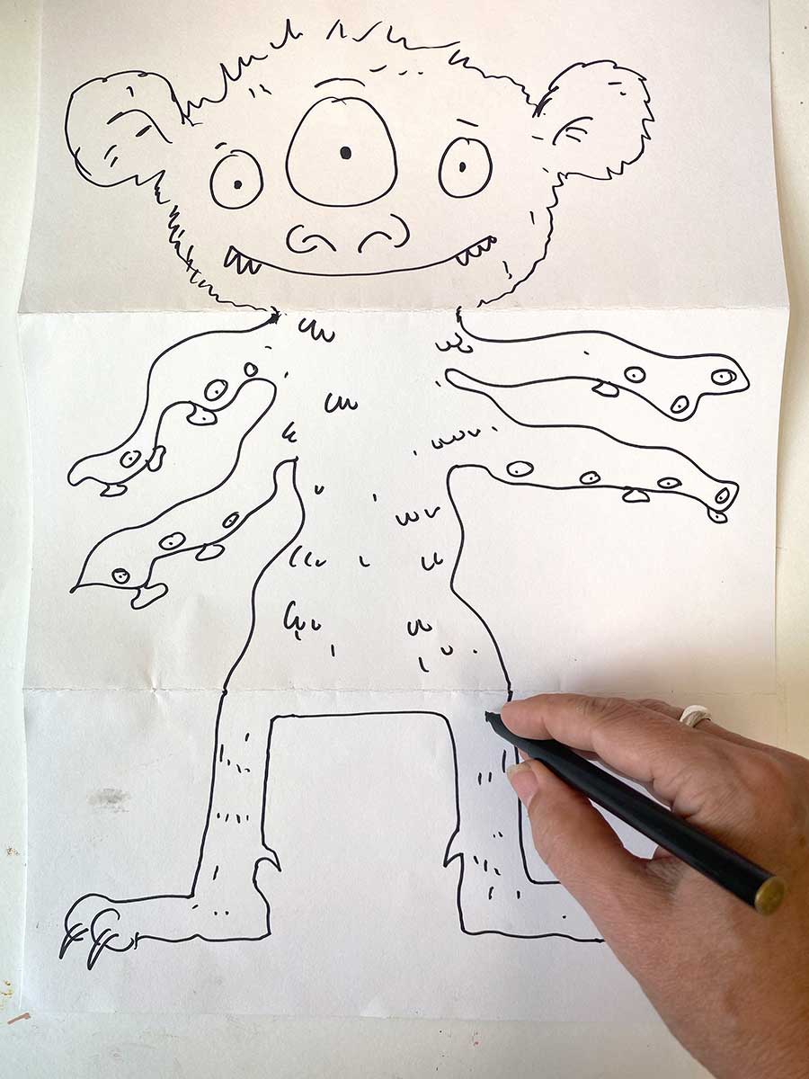 A hand sketching a mythical beast with three eyes, tentacles for arms, and clawed feet.
