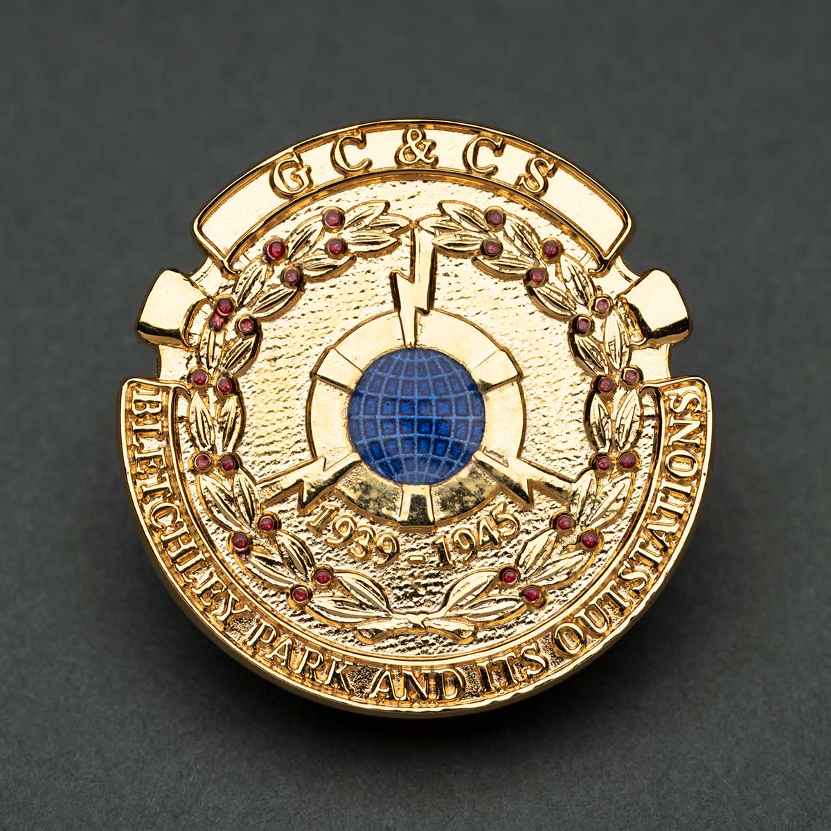 A circular gold badge with a blue globe in the centre and embossed text including 
